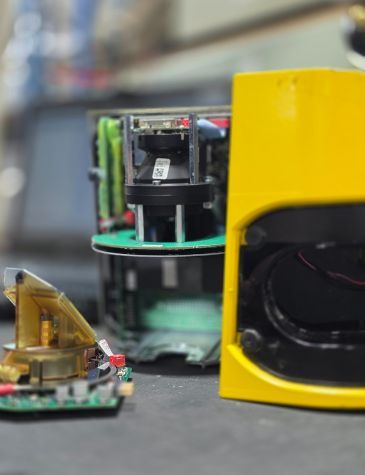 Close-up of electronic and automation equipment undergoing repairs in a workshop. A yellow device with exposed circuit boards and wiring is in the foreground, with additional green circuit boards and components visible in the background, highlighting Neutronic Technologies' expertise in electronic and automation repair services.