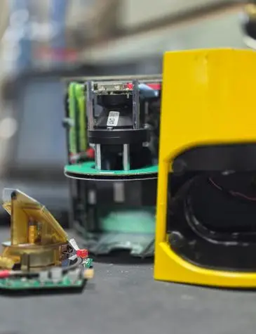 Close-up of electronic and automation equipment undergoing repairs in a workshop. A yellow device with exposed circuit boards and wiring is in the foreground, with additional green circuit boards and components visible in the background, highlighting Neutronic Technologies' expertise in electronic and automation repair services.