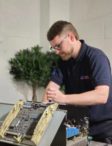 One of our engineer in a navy blue polo shirt working on a variable speed drive repairs with its internal circuit boards and wiring exposed.