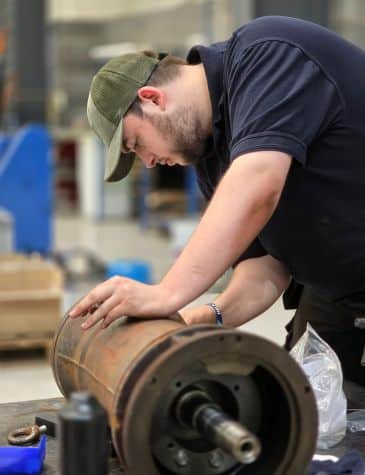 Engineer working on pump repair at Neutronic Technologies workshop, inspecting and servicing a large cylindrical pump component on a workbench.