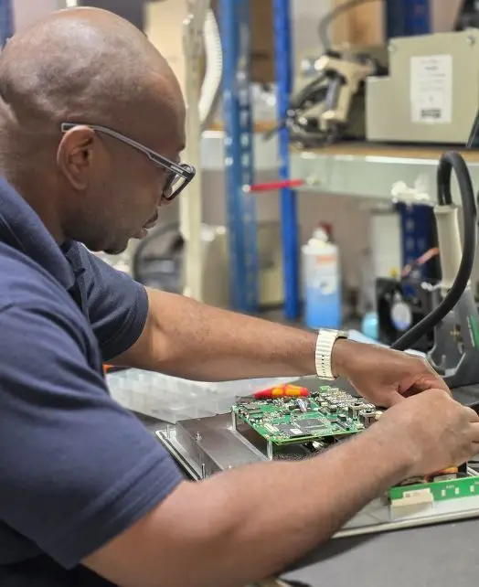 Engineer performing HMI repairs on a device's internal circuitry at a professional workstation, surrounded by electronic components and precision tools