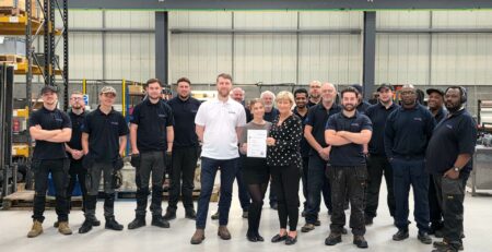 Neutronic Technologies employees in a warehouse celebrating being awarded SafeContractor Accreditation for 2025–2026, with two team members holding the certificate.