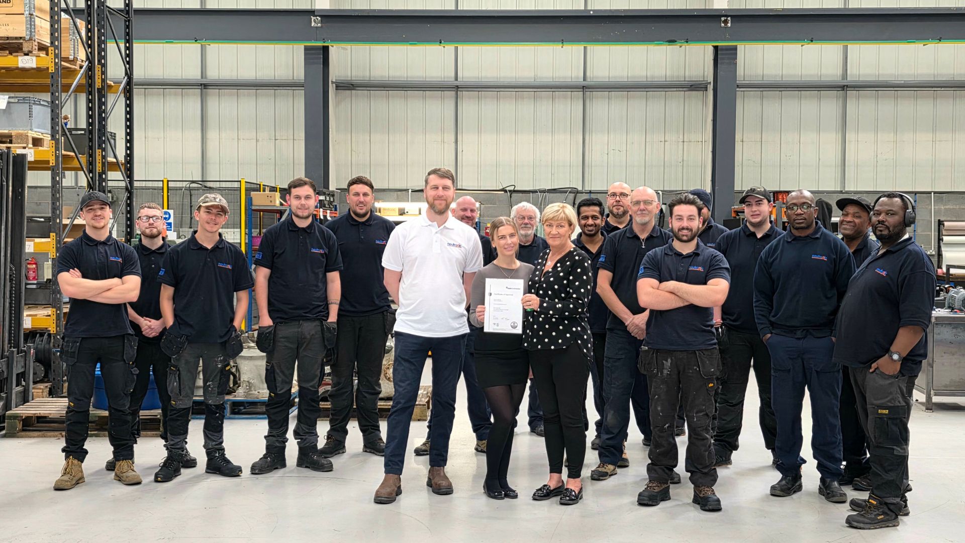 Neutronic Technologies employees in a warehouse celebrating being awarded SafeContractor Accreditation for 2025–2026, with two team members holding the certificate.