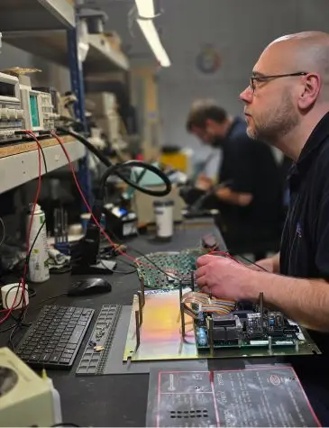 Close-up of industrial controller repairs showing precision testing of electronic components on an industrial control board by an experienced technician.